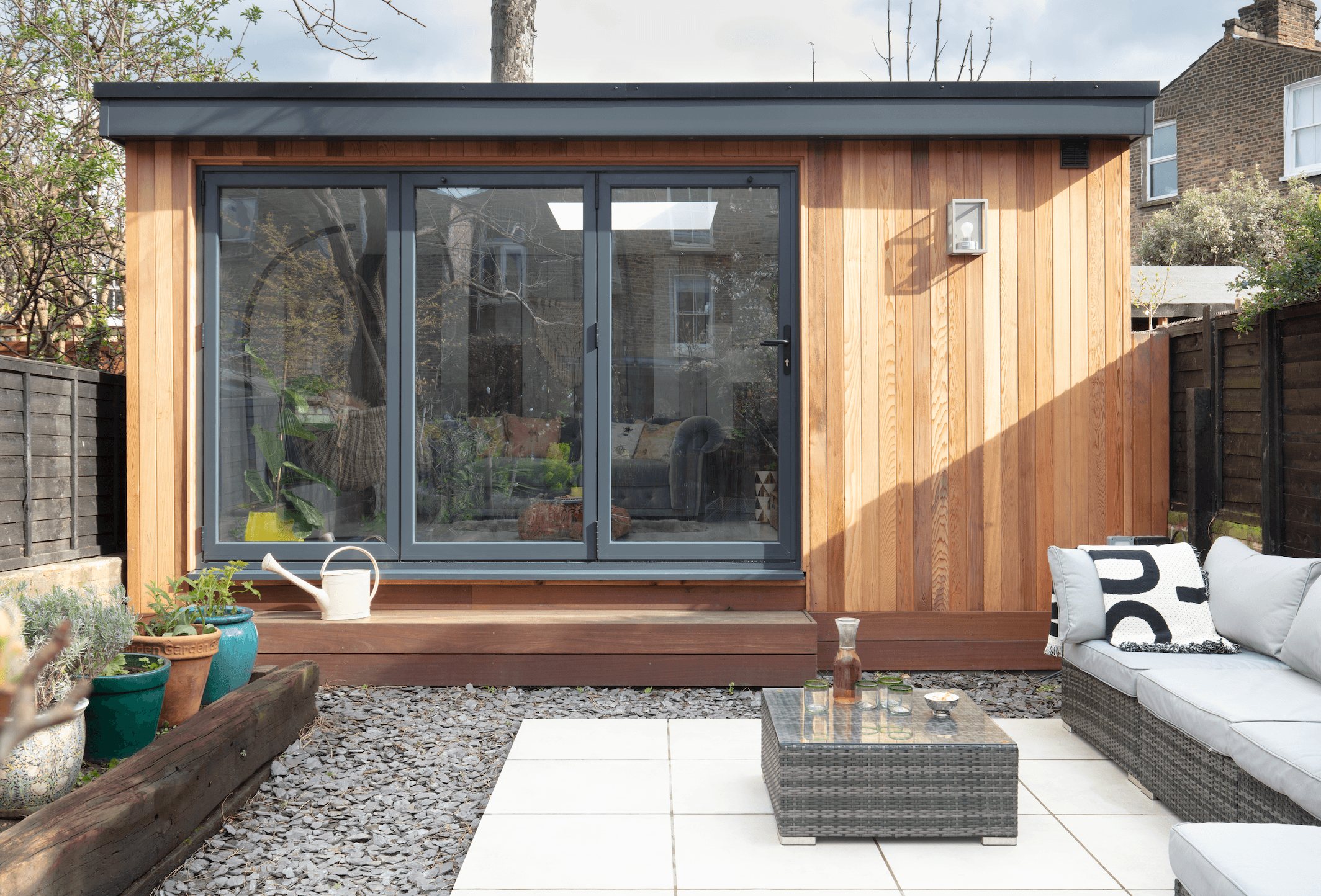Taking up the width of the garden, the grey metal doors of the garden room are softer than black and the wood adds a natural element to tie it into the surrounding plants Garden room makeover: 'Vintage touches give our modern garden room character'