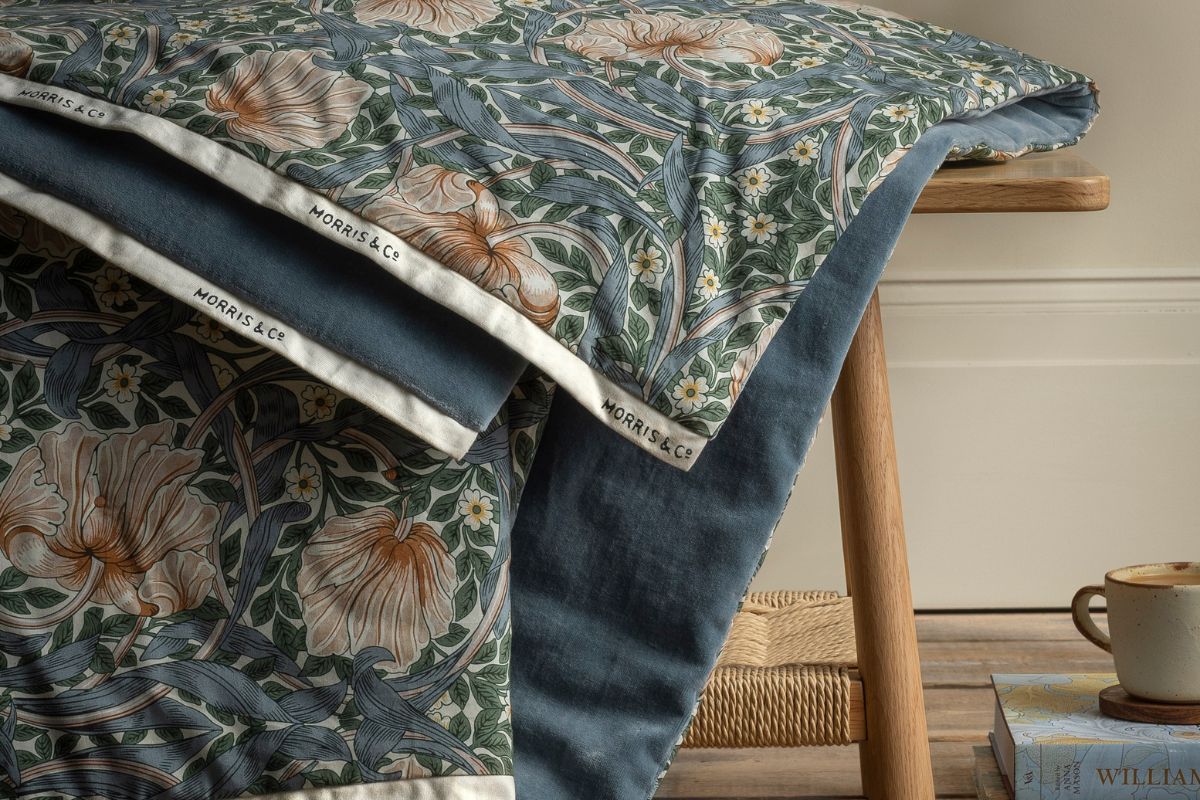 Close-up of Morris & Co quilts sat on a table with a coffee and book