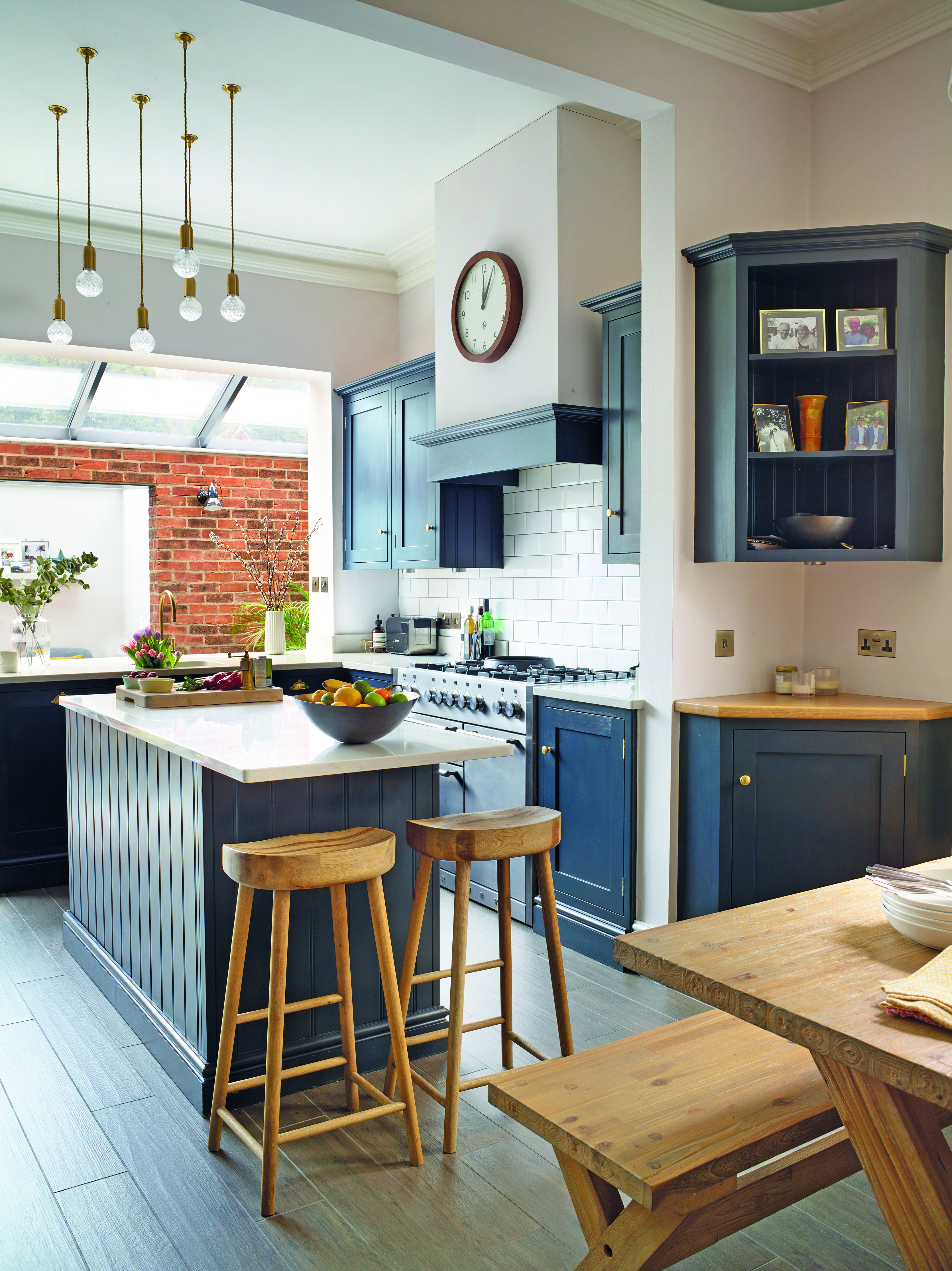 A row of skylights flood the kitchen with natural light, to make the space bright. Sarah ensures the sleek style remains homely by displaying family photographs in the open cabinetry. Wooden stools and a feature clock add a contemporary country feel A row of skylights flood the kitchen with natural light, to make the space bright. Sarah ensures the sleek style remains homely by displaying family photographs in the open cabinetry. Wooden stools and a feature clock add a contemporary country feel