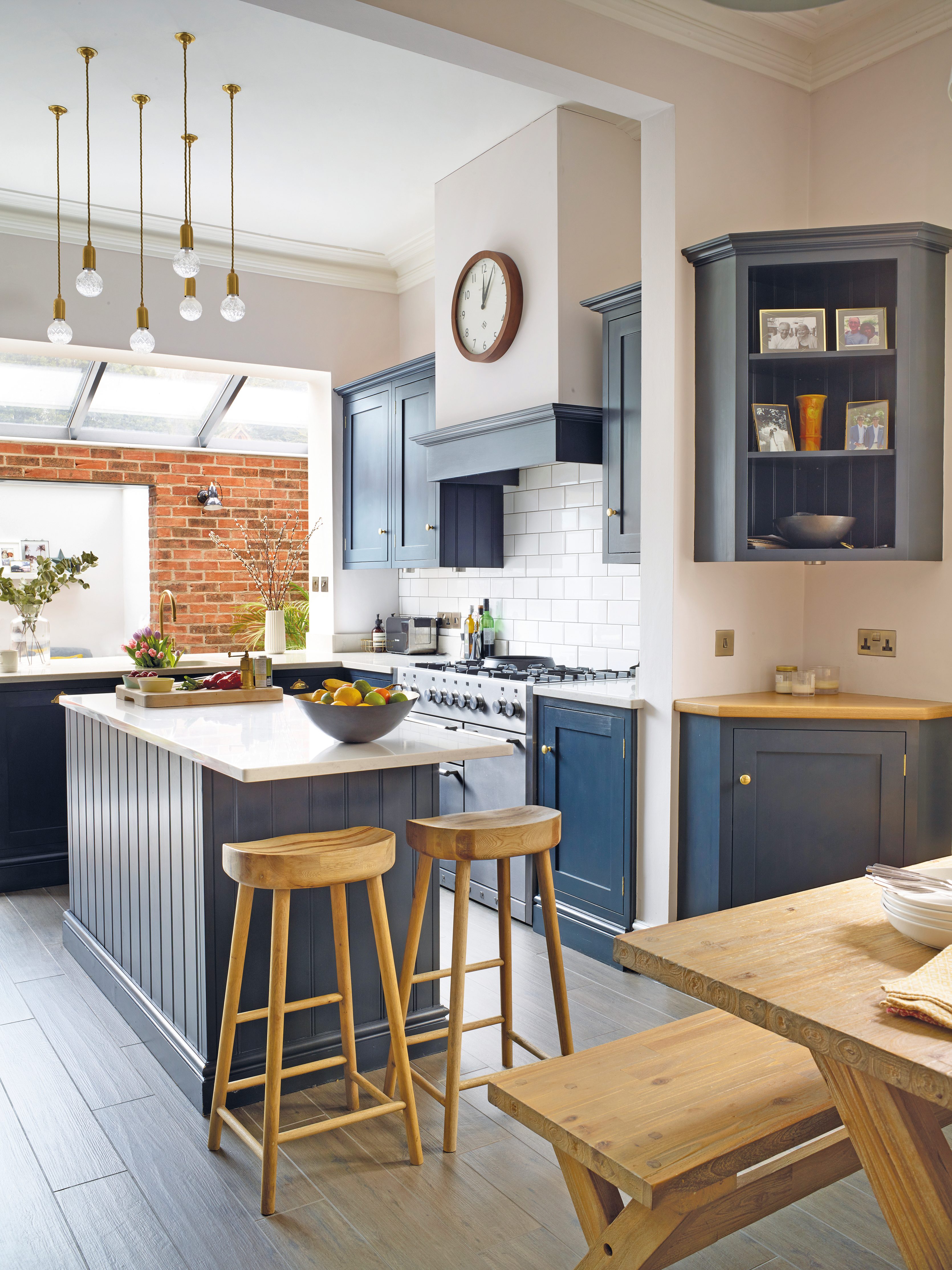 A row of skylights flood the kitchen with natural light, to make the space bright. Sarah ensures the sleek style remains homely by displaying family photographs in the open cabinetry. Wooden stools and a feature clock add a contemporary country feel A row of skylights flood the kitchen with natural light, to make the space bright. Sarah ensures the sleek style remains homely by displaying family photographs in the open cabinetry. Wooden stools and a feature clock add a contemporary country feel