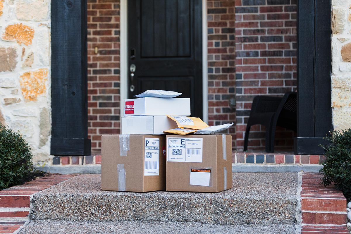 A stack of packages are on the front step of a house.
