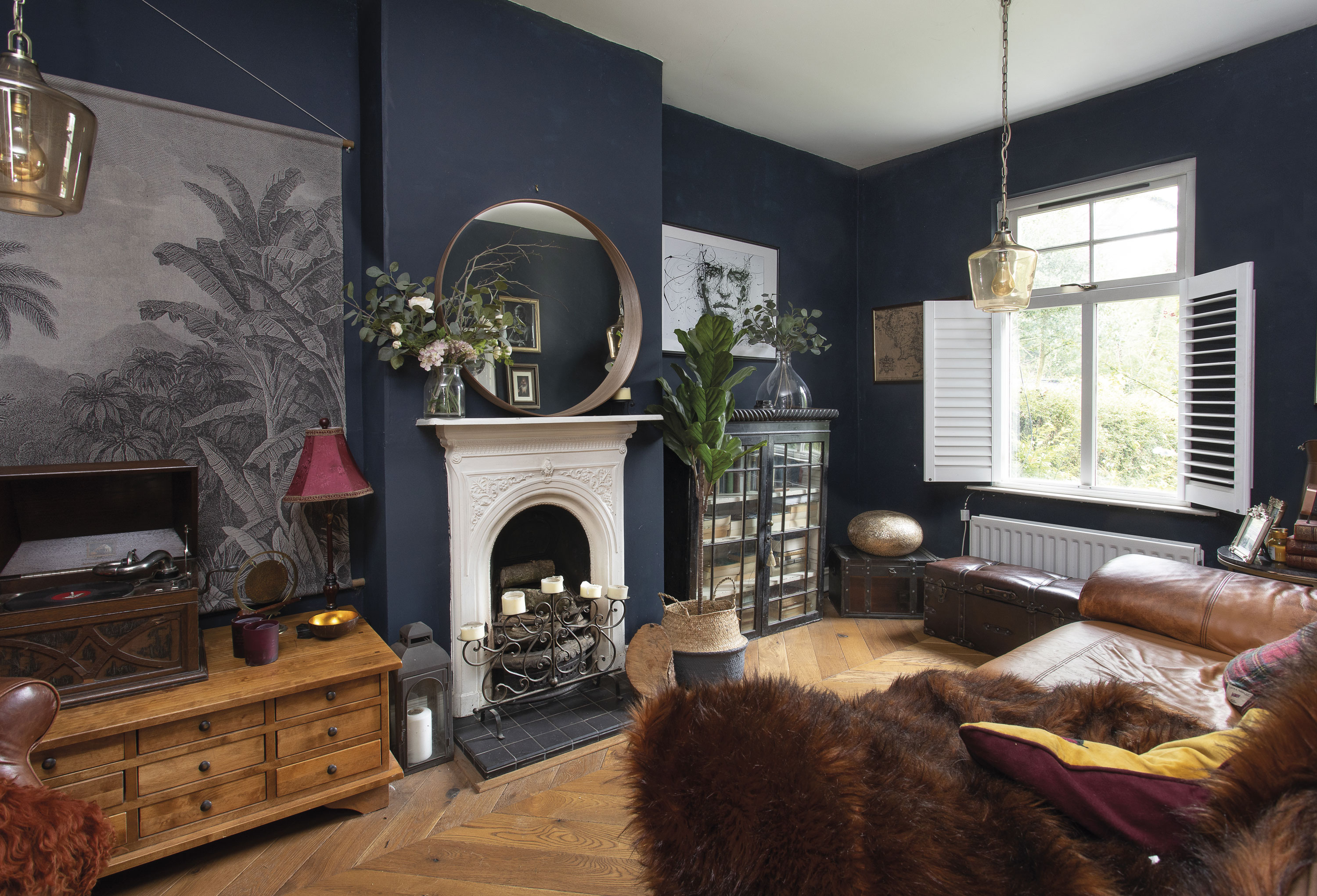 ‘This is where we watch movies. We have a projector and snuggle up with the dogs with the shutters closed and the fire on,’ Eniko shares. ‘The engineered wood flooring laid in chevrons is practical for the dogs, as they do scratch sometimes.’ It’s finished with walls painted in Basalt by Little Greene, a round mirror from IKEA and a pencil-drawn portrait from Desenio ‘This is where we watch movies. We have a projector and snuggle up with the dogs with the shutters closed and the fire on,’ Eniko shares. ‘The engineered wood flooring laid in chevrons is practical for the dogs, as they do scratch sometimes.’ It’s finished with walls painted in Basalt by Little Greene, a round mirror from IKEA and a pencil-drawn portrait from Desenio